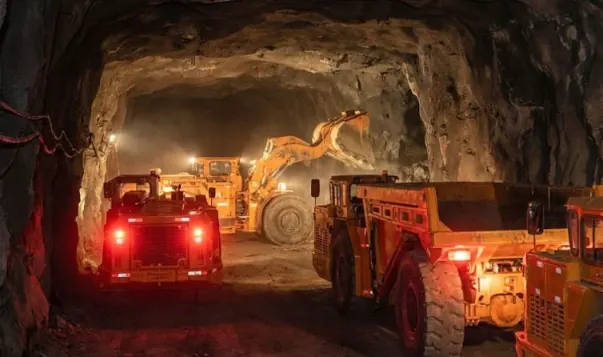 heavy congestion of orange underground mining transport vehicles in a narrow tunnel, illustrating the queue trap where dump trucks wait for a loader due to inefficient haulage system mat