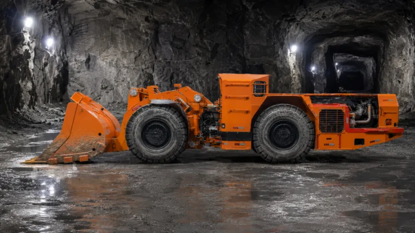 Side view of an orange heavy-duty loader parked in a well-lit mine shaft